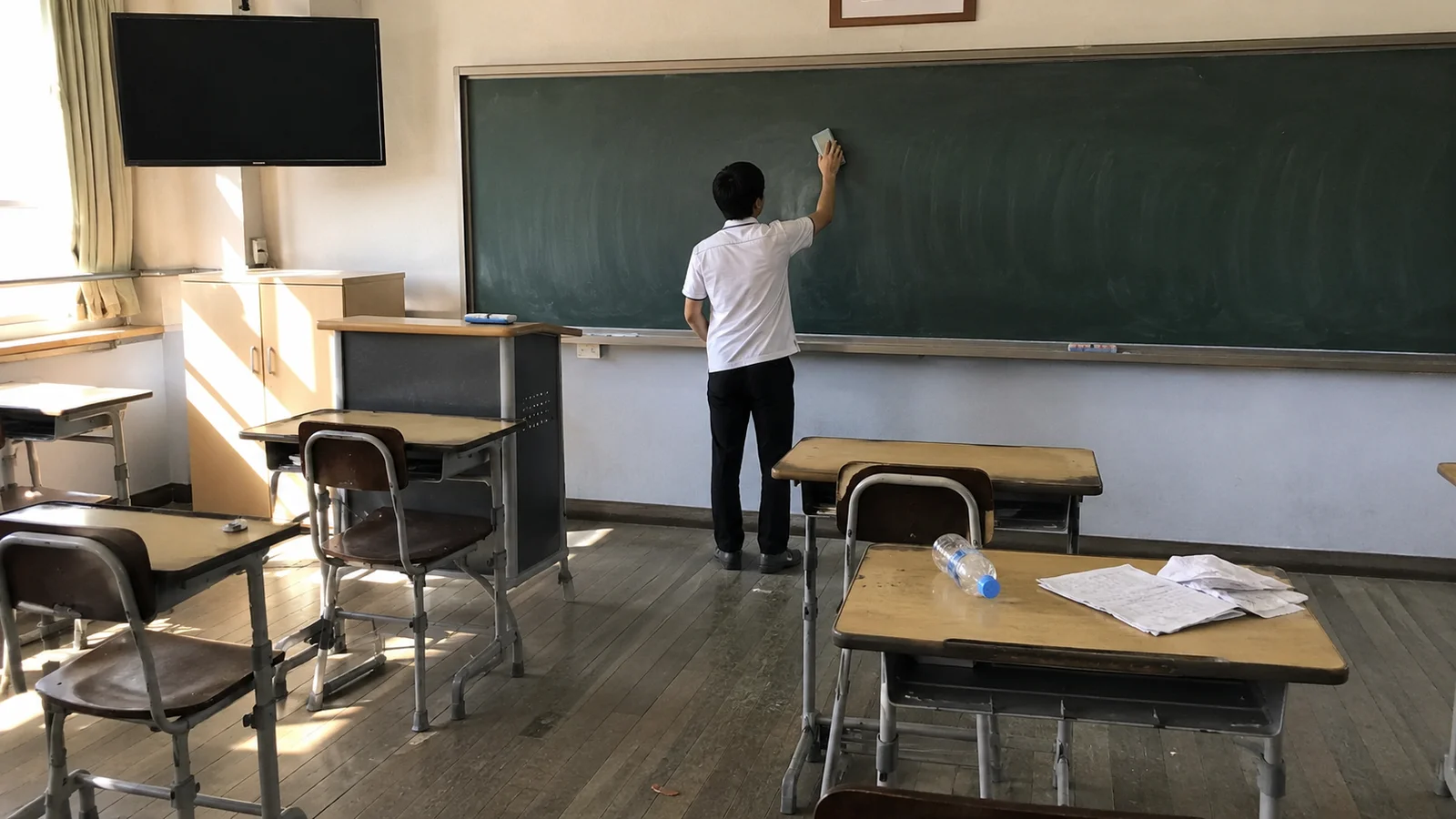 오후 햇살이 드는 빈 교실에서 칠판을 닦고 있는 남학생의 뒷모습