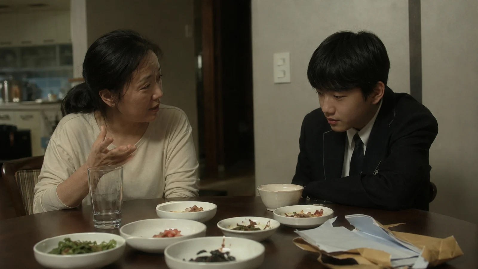 저녁 식탁 모퉁이에 마주 앉아 아들과 심각하게 대화하는 한국인 어머니