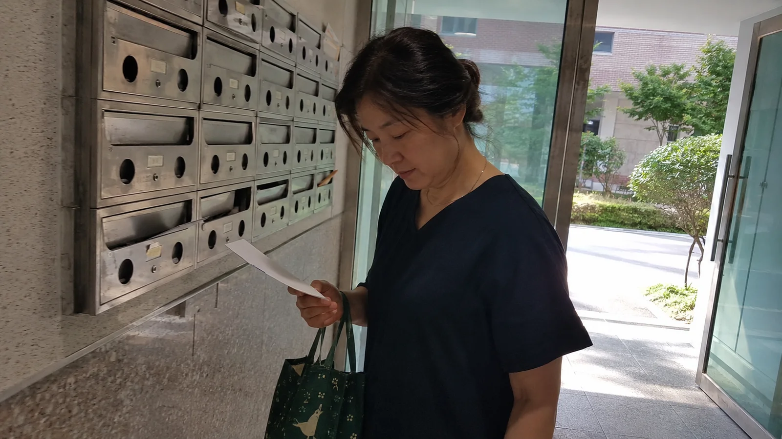 아파트 공동현관 우편함에서 학교가 보낸 봉투를 꺼내 확인하는 한국인 어머니