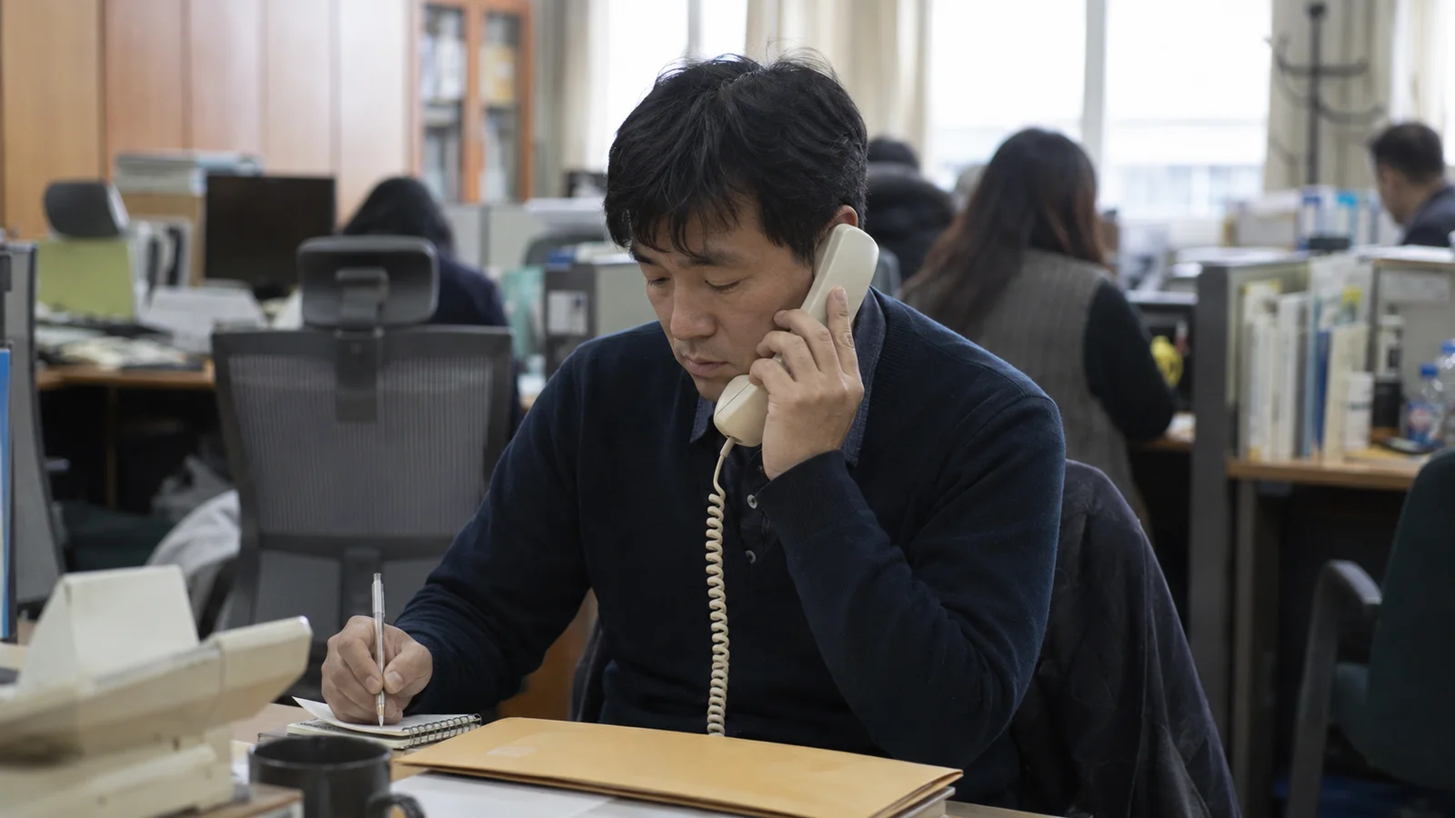 방과 후 한국 학교 교무실에서 수화기를 들고 통화하며 메모하는 교사