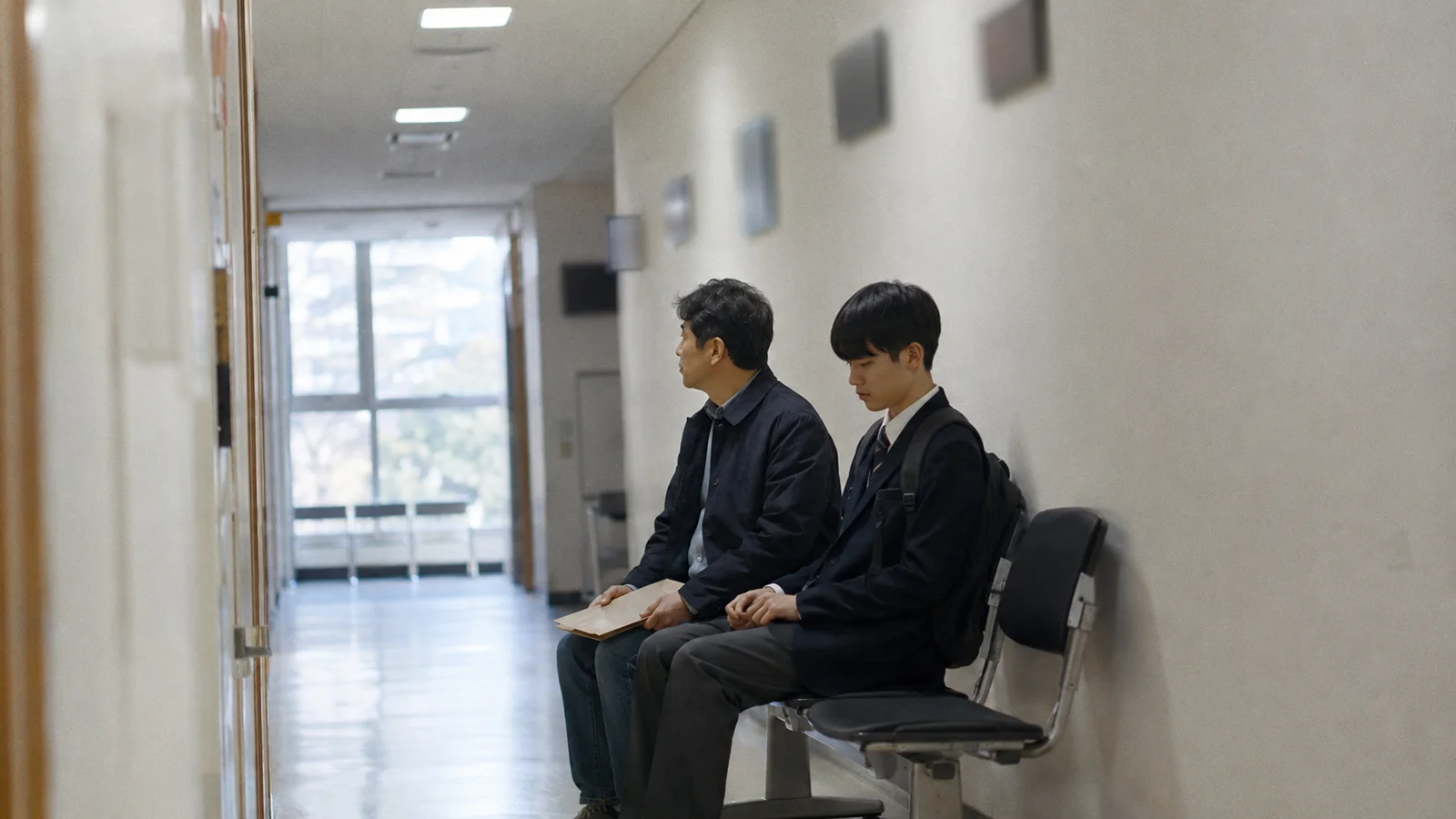 교육지원청 복도 의자에 나란히 앉아 차례를 기다리는 아버지와 교복 입은 아들