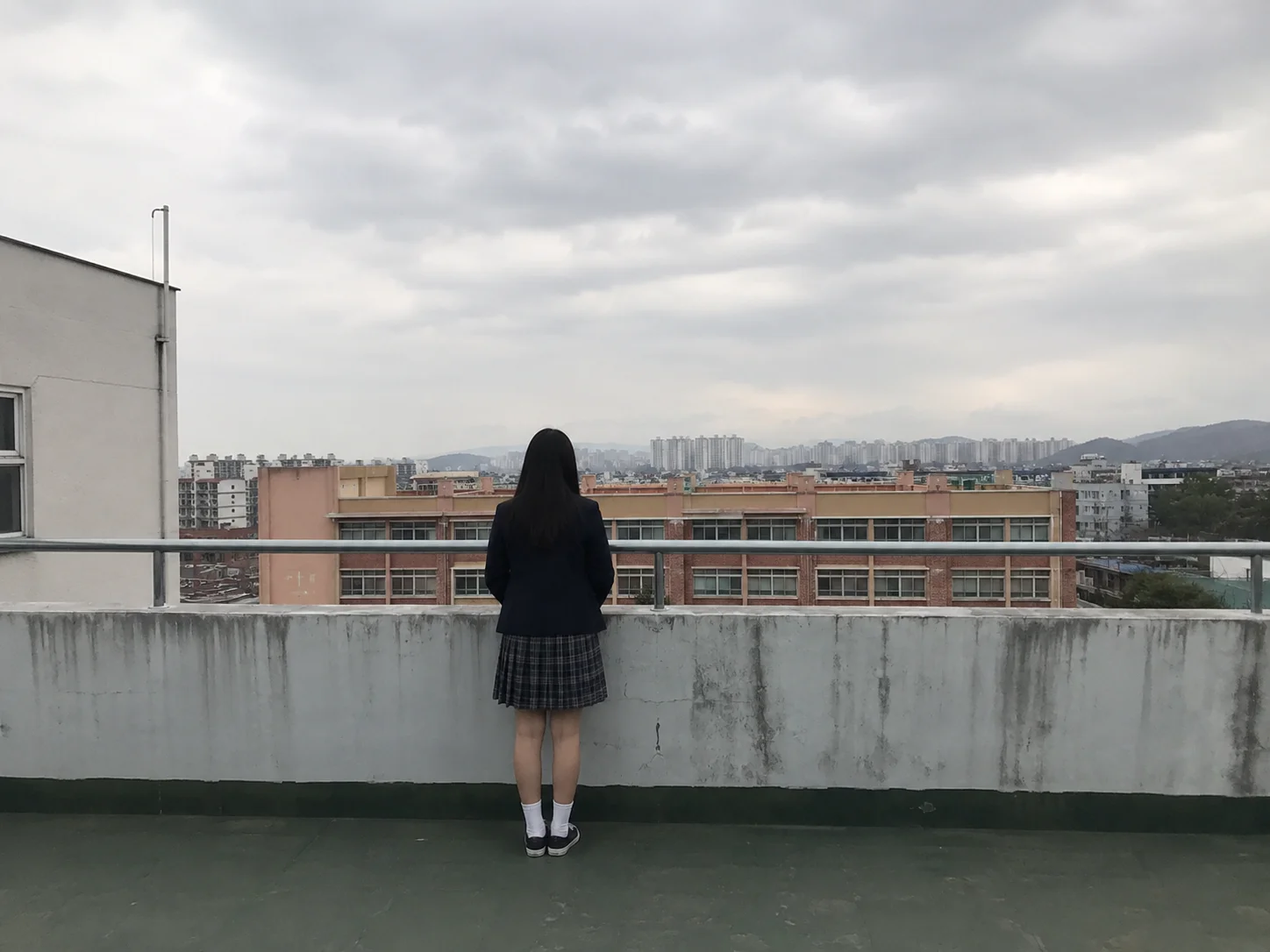 학교 옥상 난간 앞에 홀로 선 학생의 뒷모습
